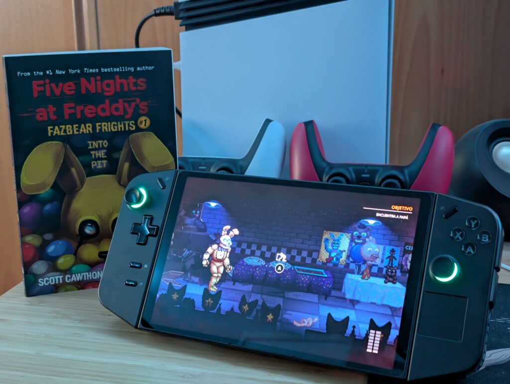 La Legion Go con Into the Pit en marcha, junto al libro Fazbear Frights