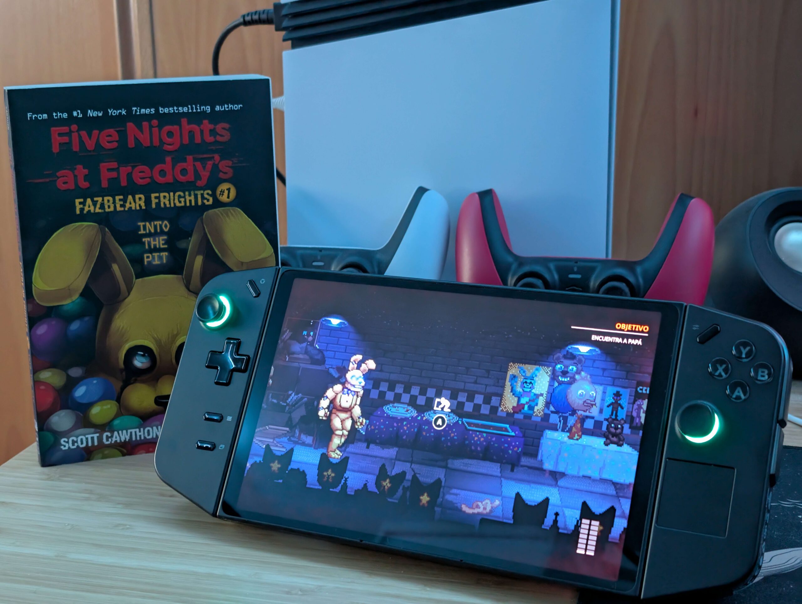 La Legion Go con Into the Pit en marcha, junto al libro Fazbear Frights